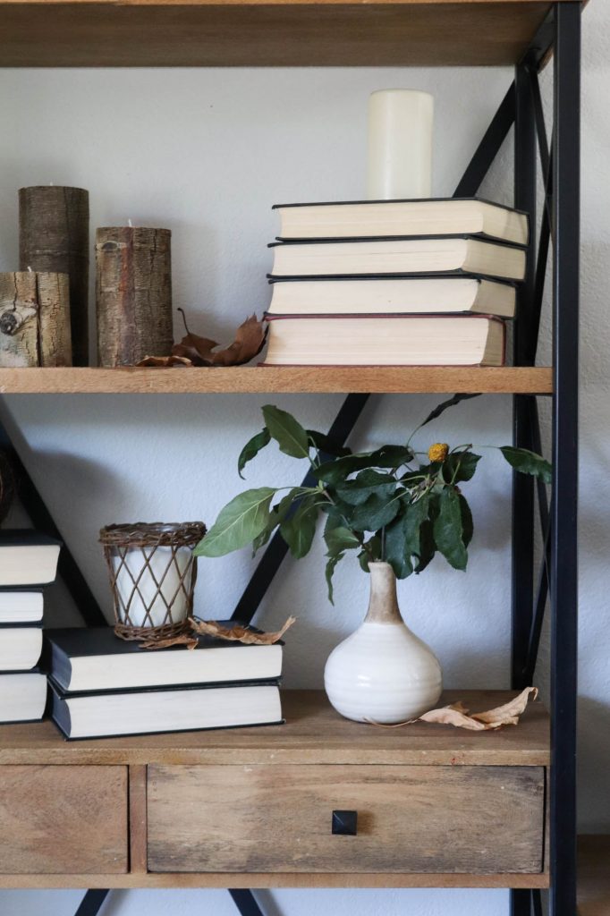 A picture of open shelving with books, candles and leaves.