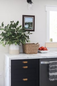 A picture of a kitchen with art hanging on the wall and a vase filled with tree branches.