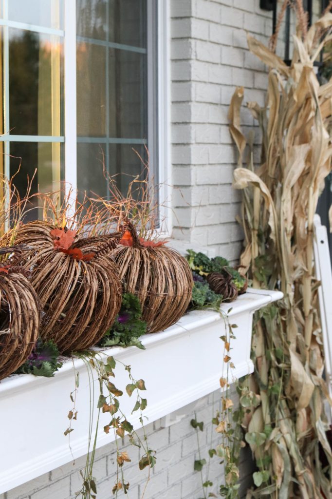 A picture of a large window box with wicker pumpkins and flowering kale with ivy coming over the sides. 