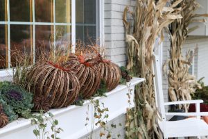 A picture of wicker pumpkins and flowering kale in a white window box.