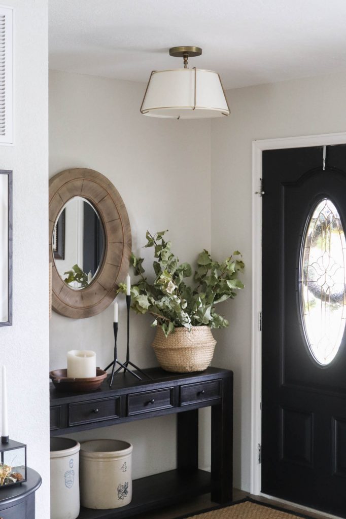 A picture of an entry with a hanging light fixture, side table and black front door. 