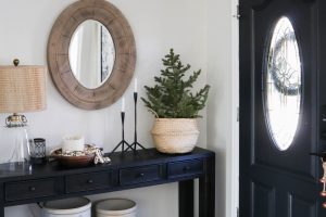 A picture of an entry way with a large mirror and a mini Christmas tree in a basket.