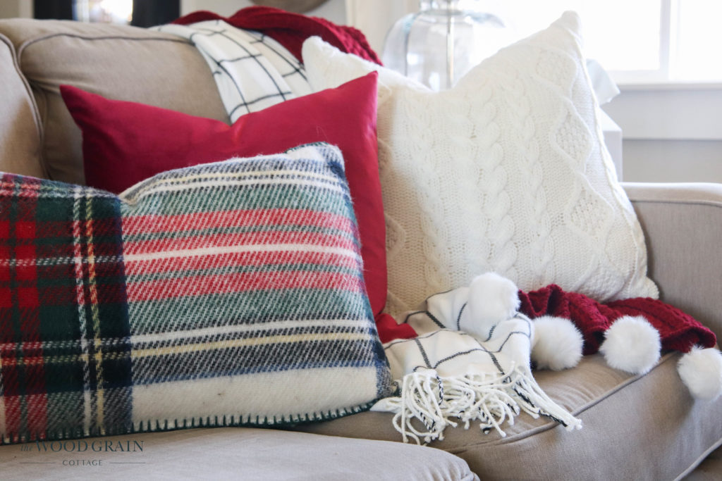 A picture of red, cream and plaid pillows on a couch. 